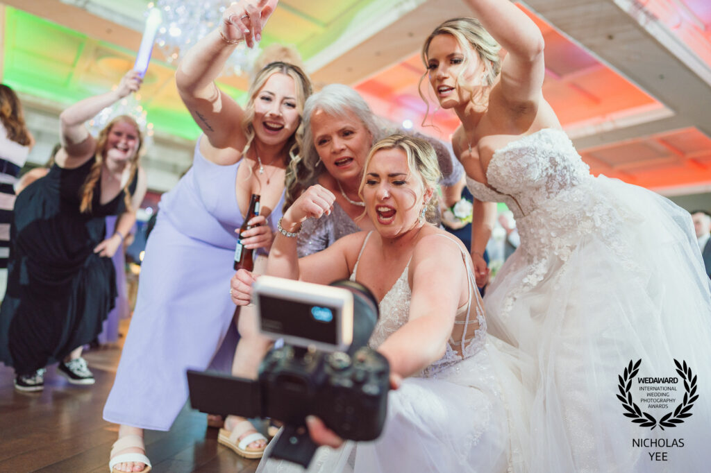 Group of joyful women in wedding attire taking a lively selfie at a celebration, showcasing candid moments and fun, part of the WedAward Collection.