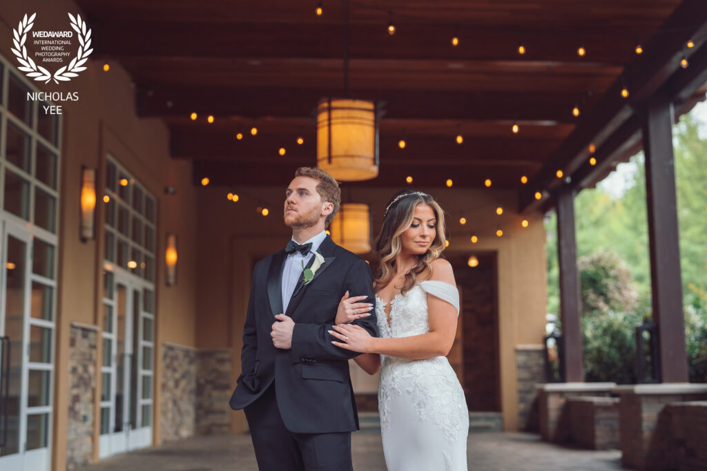 Bride and groom posing elegantly under warm string lights in an outdoor covered walkway, part of the WedAward Collection #92.