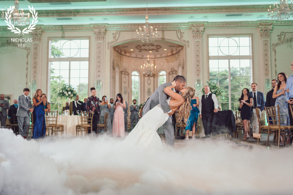 Bride and groom sharing a dramatic first dance surrounded by a cloud of fog in an elegant ballroom filled with guests, part of the WedAward Collection #95.