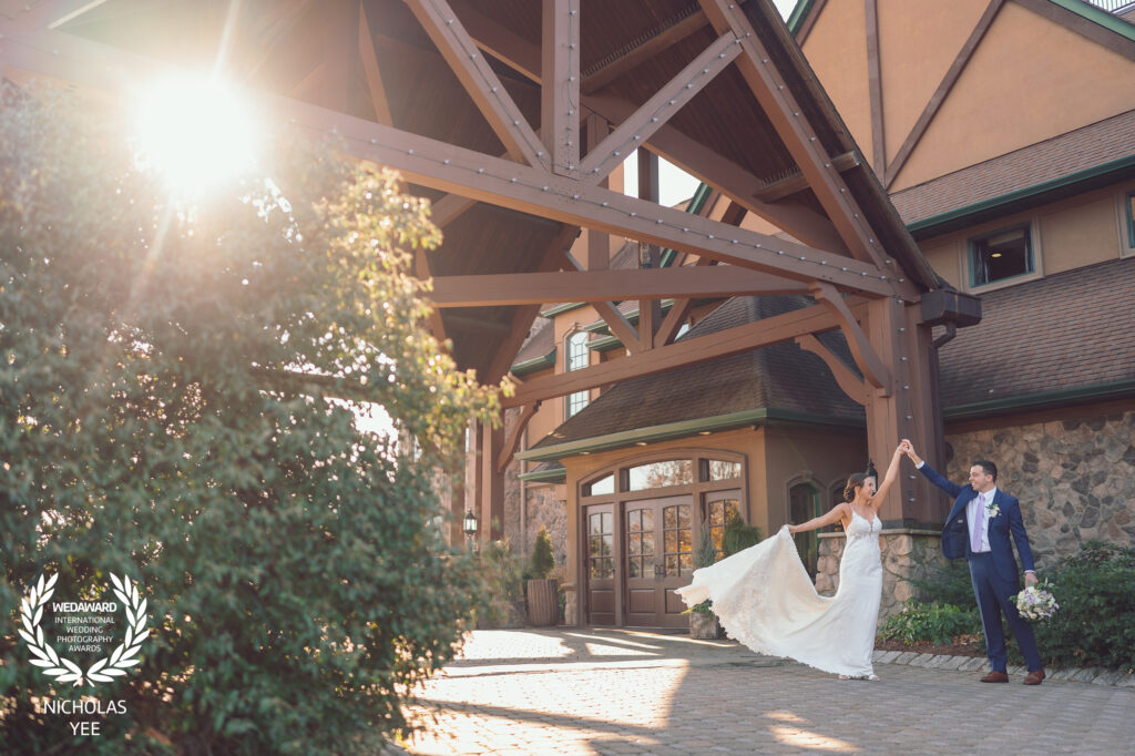 Bride and groom dancing joyfully under a wooden pavilion with sunlight streaming through the trees, part of the WedAward Collection #99.