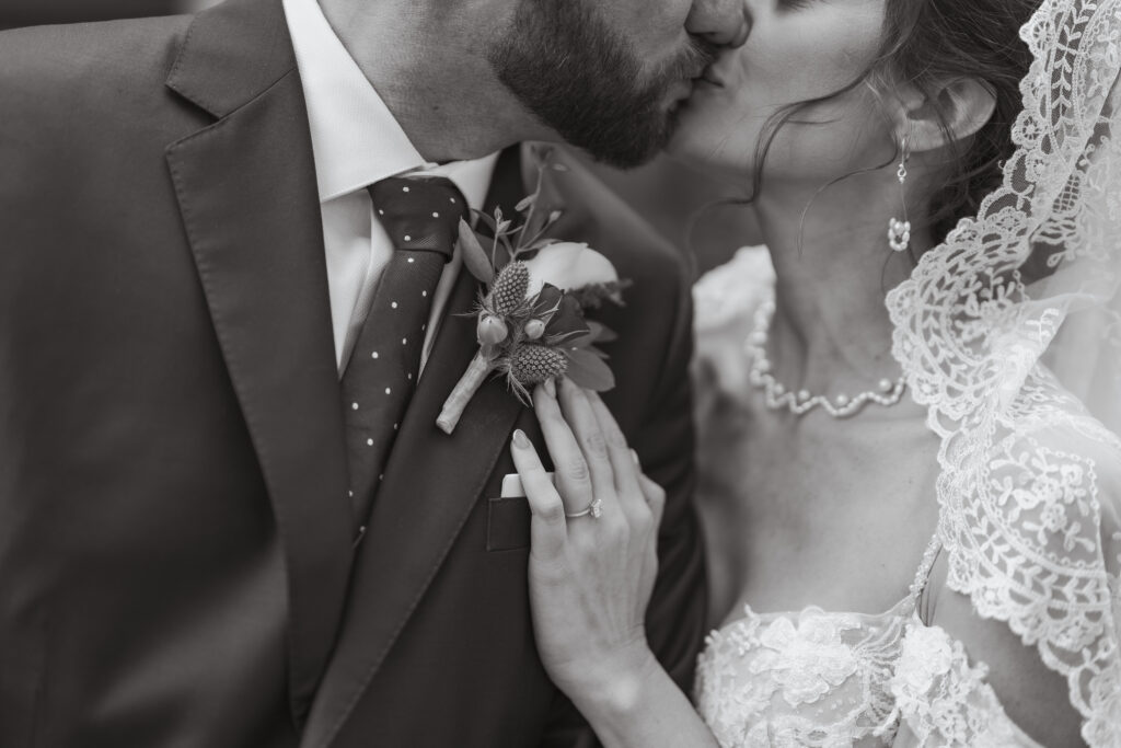 A close-up black-and-white photo of a bride and groom sharing a tender kiss, highlighting the bride’s lace veil, pearl necklace, and engagement ring, beautifully captured by Nicholas Yee Photography with no hidden fees or extra charges.