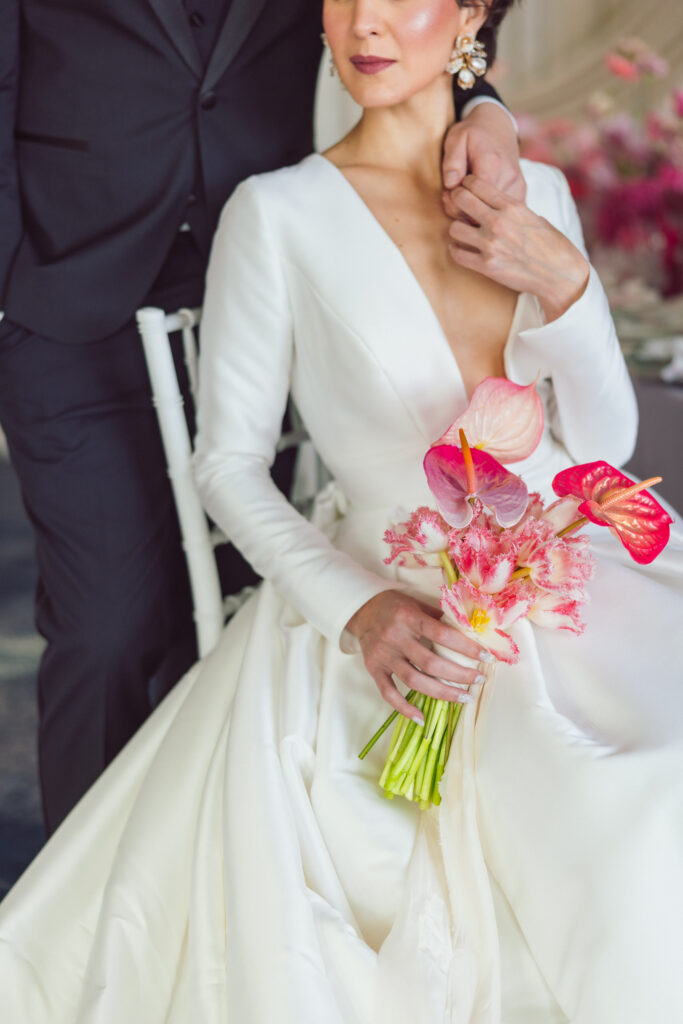 Close-up of a bride in a white gown holding a bouquet of pink and red flowers, with the groom’s arm resting on her shoulder, showcasing the quality and style of Nicholas Yee Photography with no hidden fees or extra charges.