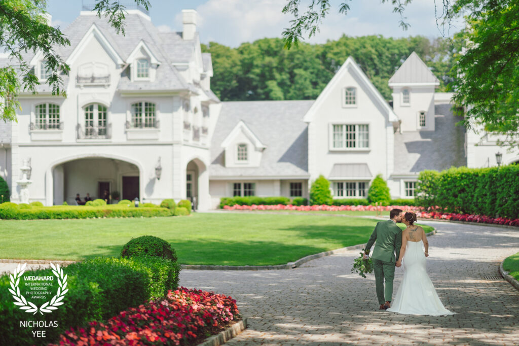 Couple walking hand-in-hand in front of a grand estate, captured in an award-winning moment by New Jersey wedding photographer Nicholas Yee. The lush garden and elegant venue create a perfect backdrop for this romantic scene.