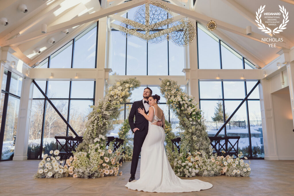 A bride and groom standing confidently in front of a breathtaking floral backdrop in a modern venue, captured by an award-winning wedding photographer.