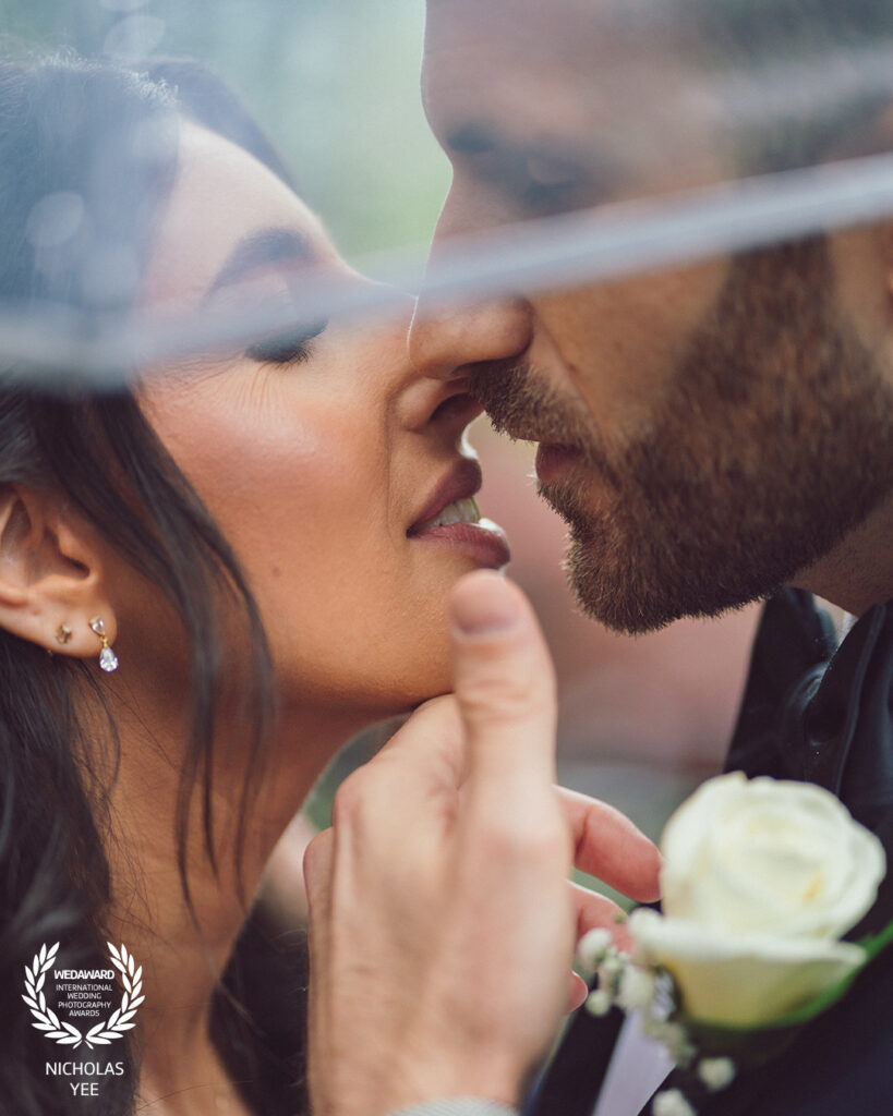 Wedisson Collection 135 winning wedding photo by Nicholas Yee Photography featuring a bride and groom sharing an intimate umbrella kiss in a close, romantic portrait.